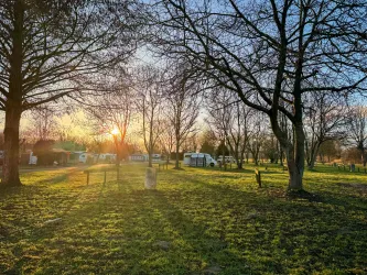 Ein Campingplatz mit einem detaillierten Lageplan und verschiedenen Stellplätzen. Im Vordergrund ist eine Familie vor einem Zelt zu sehen, die die Natur genießt.