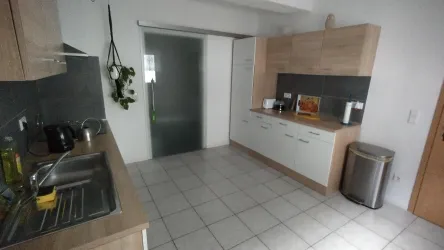 Eine moderne Küche mit hellen Holzschränken und grauen Fliesen. Das Fenster sorgt für viel Licht und eine freundliche Atmosphäre.
