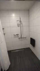Eine moderne Dusche mit weißen Fliesen und einer Handbrause. Der Boden ist in dunklem Holzoptik gehalten.