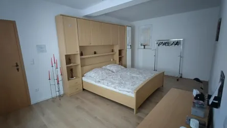 Ein modernes Schlafzimmer mit einem großen Bett, einem Holzkasten und einem einfachen Sideboard. Der Raum hat helle Wände und einen gepflegten Holzfußboden.