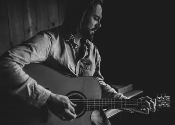 Ein Mann spielt Gitarre in einem dunklen Raum. Die Atmosphäre ist ruhig und nachdenklich.
