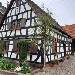 Eine metallene Figur eines Wanderers steht in einem kleinen Garten. Im Hintergrund sieht man ein traditionelles Fachwerkhaus.