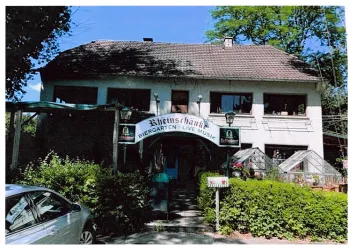 Ein gemütliches Gasthaus mit einem Biergarten im Freien. Die Fassade ist von Pflanzen umgeben und es gibt Schilder für Live-Musik.