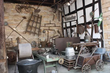 Ein historischer Geräteschuppen mit verschiedenen landwirtschaftlichen Werkzeugen und Maschinen. Die Wände sind mit alten Werkzeugen dekoriert, die die ländliche Vergangenheit zeigen.