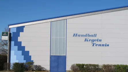 Ein modernes Sportgebäude mit blauer und grauer Fassade. Auf der Wand sind die Sportarten Handball, Kegeln und Tennis aufgeschrieben.