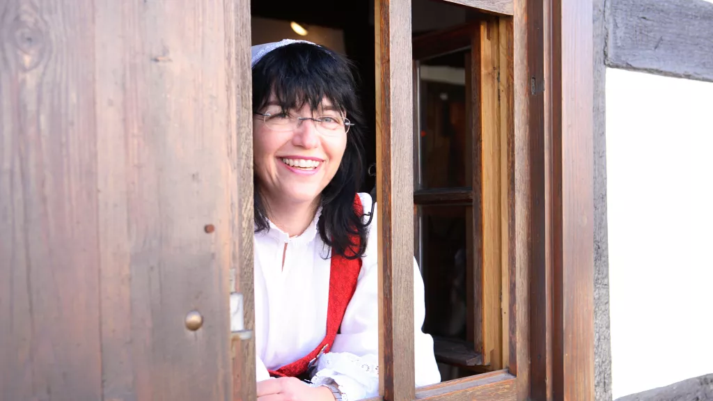 Frau in Tracht schaut aus dem Fenster